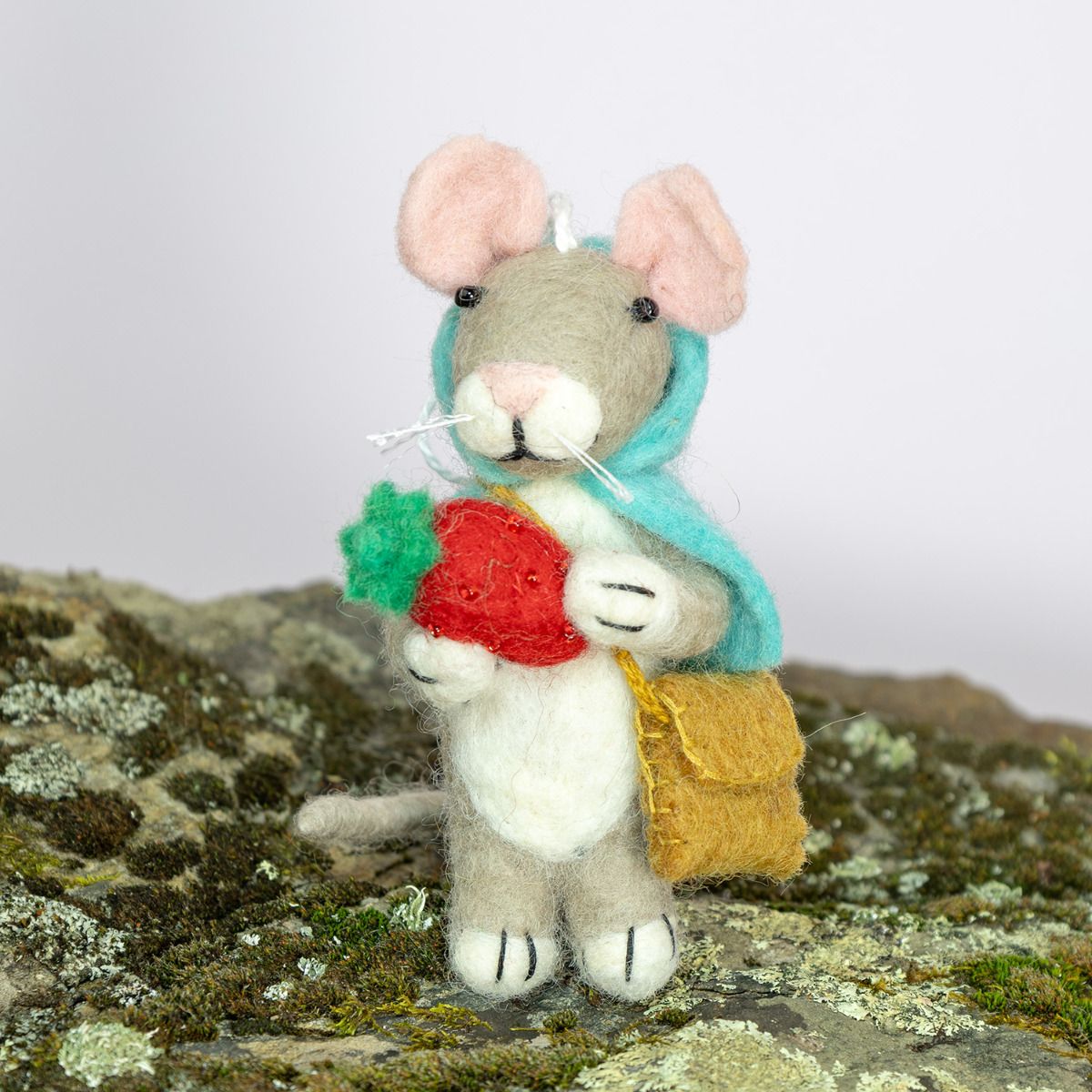 Felt mouse ornament with a green scarf, red strawberry, and yellow backpack on a mossy background