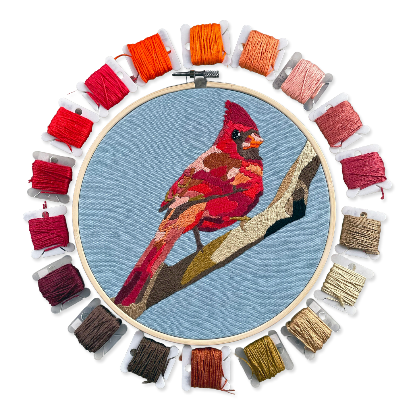 Embroidery hoop with a red cardinal bird design surrounded by colorful threads on a white background