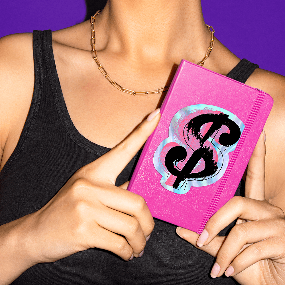 Woman holding a notebook featuring a sticker of Andy Warhol's $.