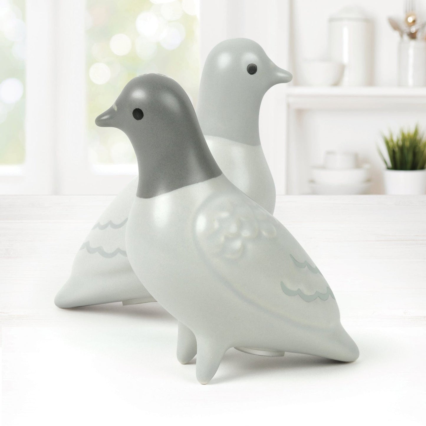 Two ceramic pigeon salt & pepper shaker figurines on a white surface with a blurred indoor background
