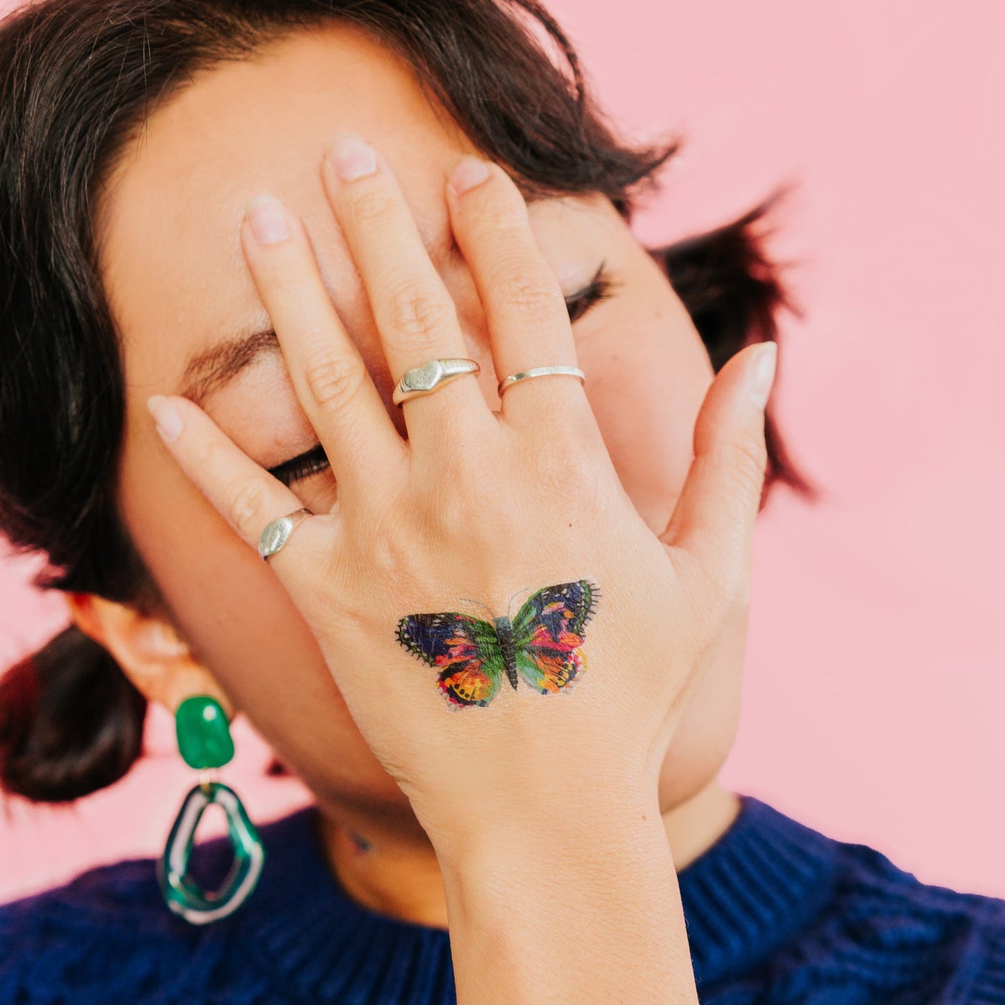 Person with a butterfly tattoo on their hand against a pink background