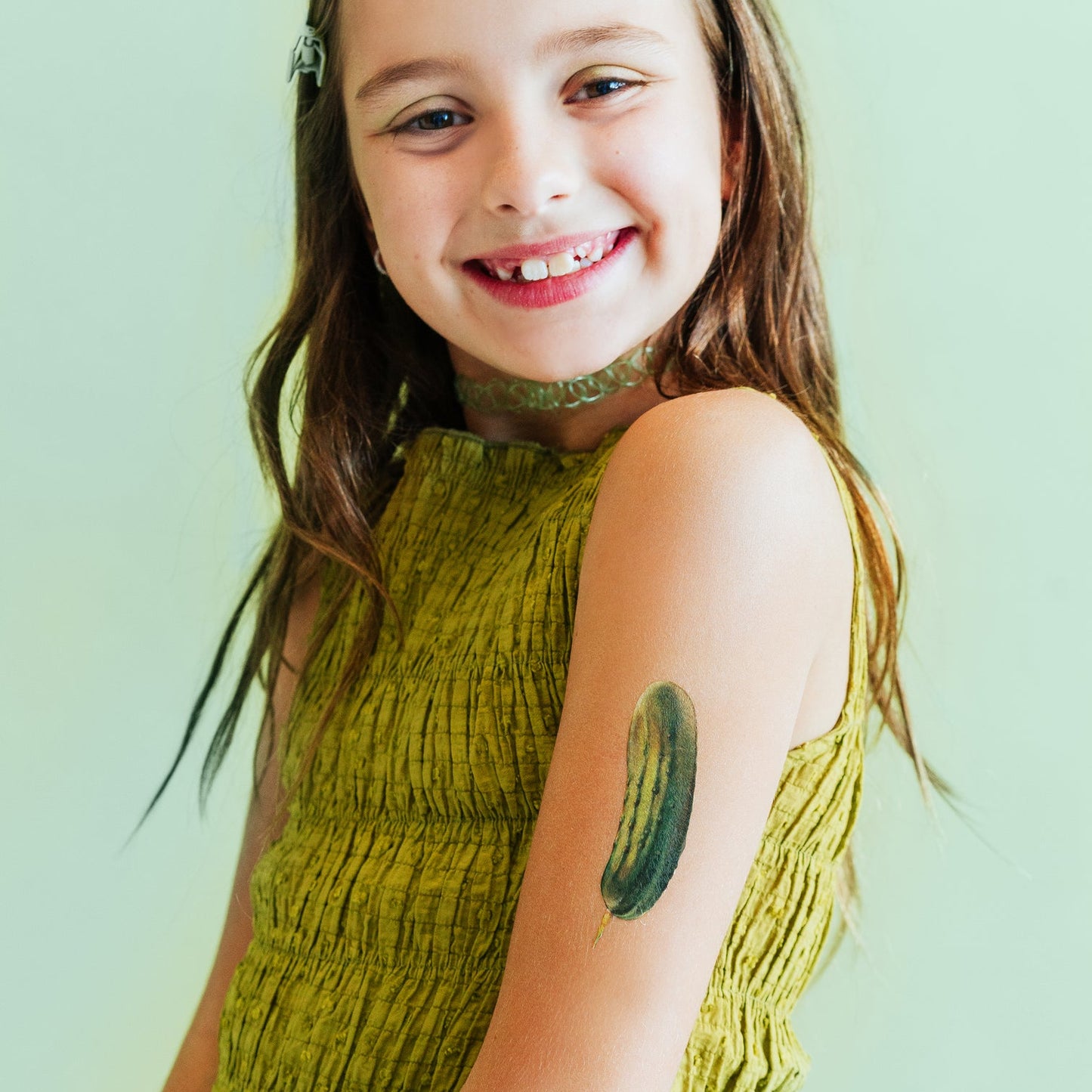 Young girl with a green dress and pickle tattoo on a light green background