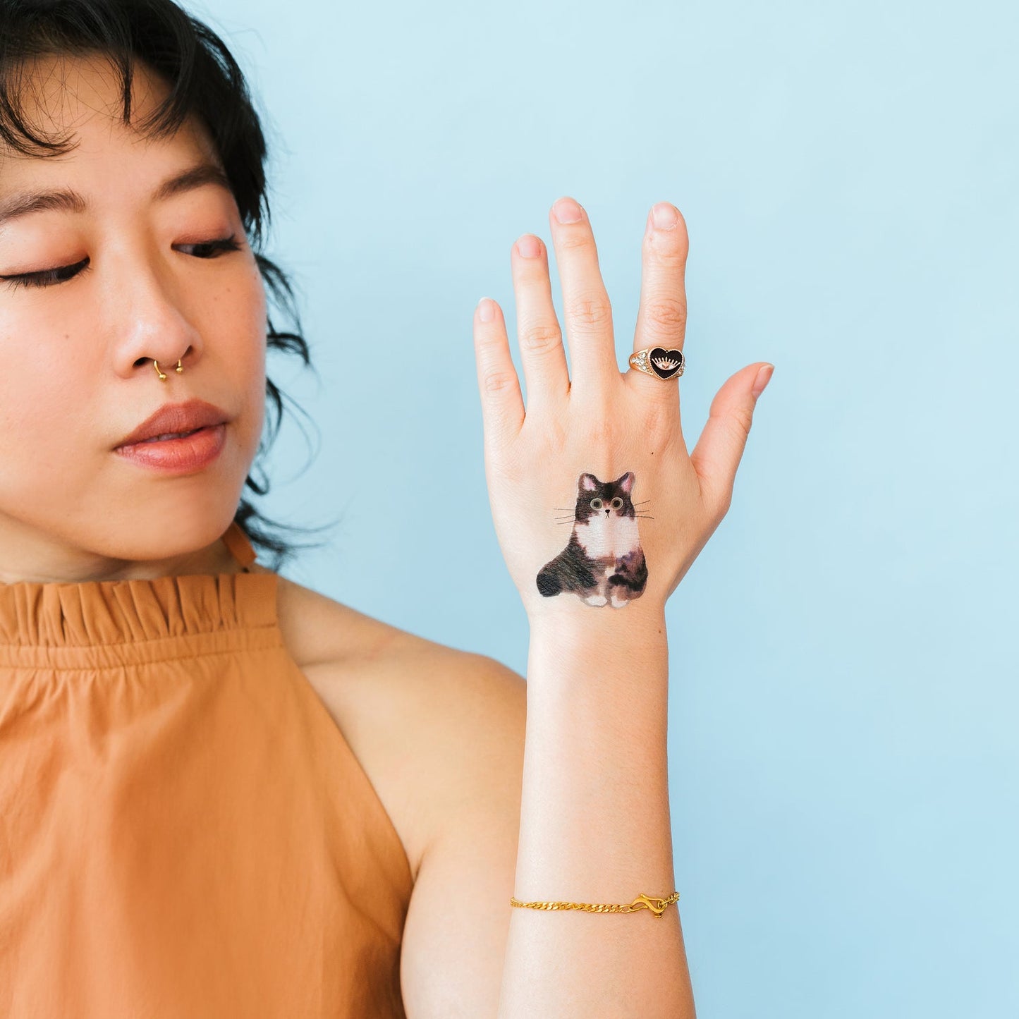 Woman wearing a cat-themed temporary tattoo on her wrist against a light blue background