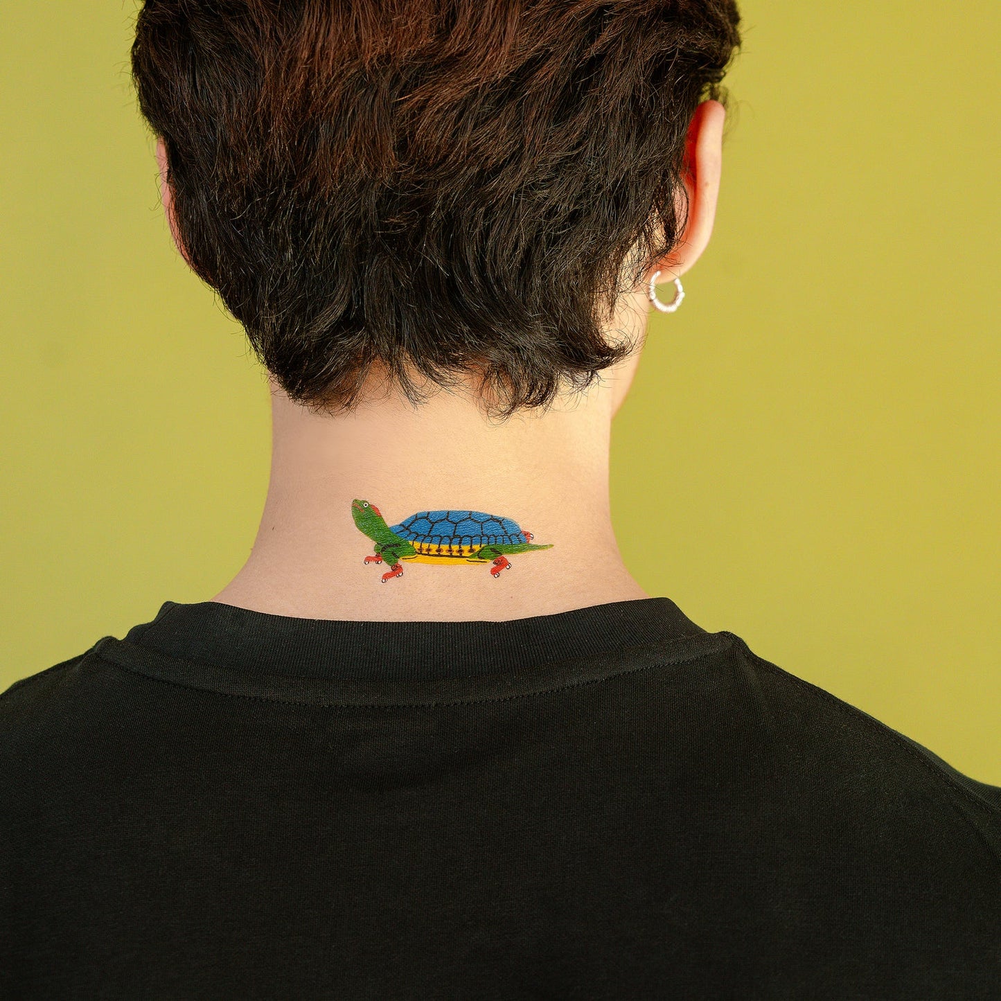 Person with a colorful turtle tattoo on their neck against a green background