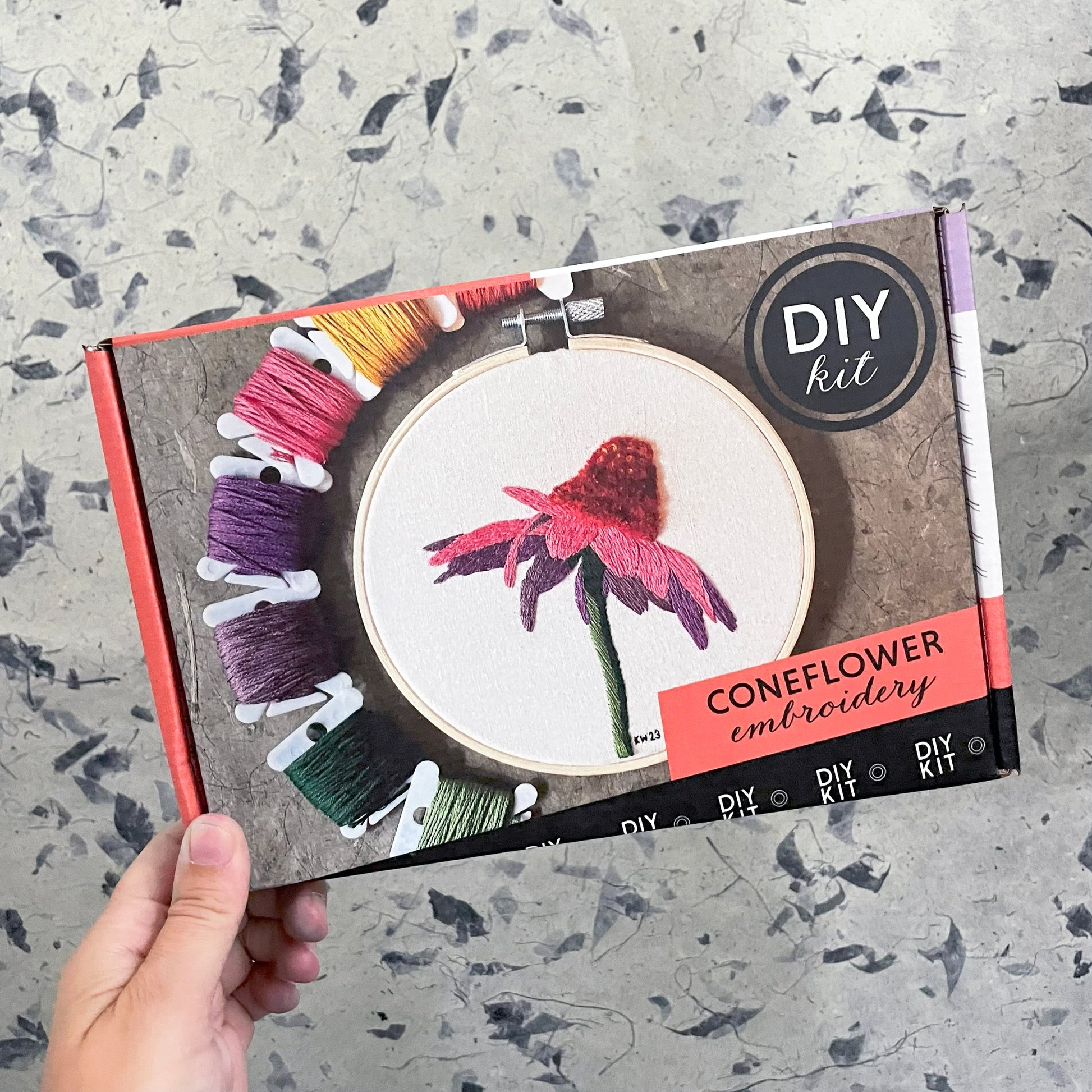 DIY coneflower embroidery kit held by a hand on a textured surface
