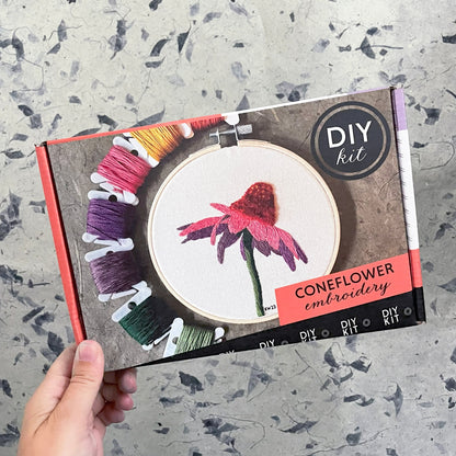 DIY coneflower embroidery kit held by a hand on a textured surface