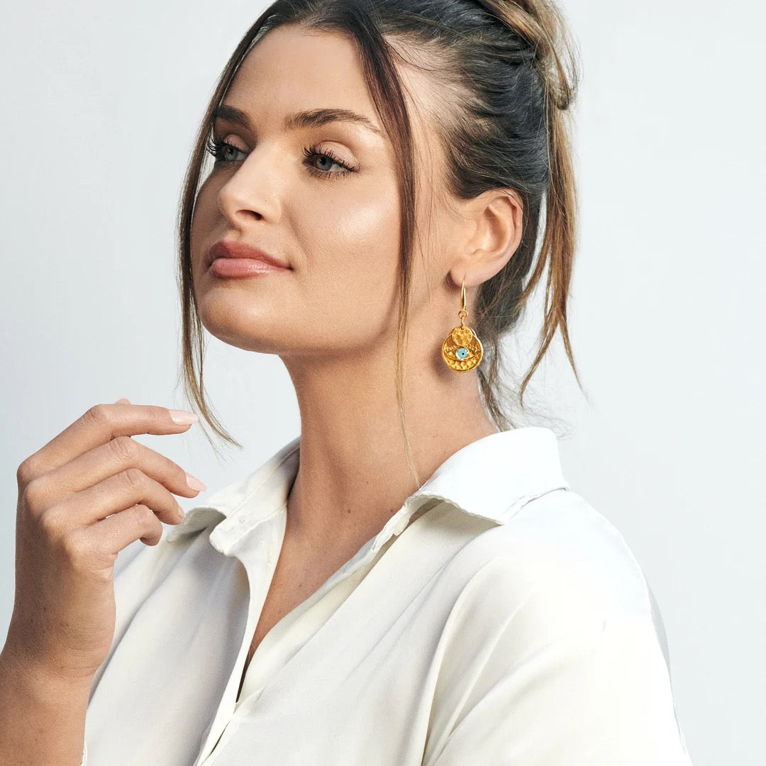 Woman wearing gold earrings with a white shirt on a light gray background