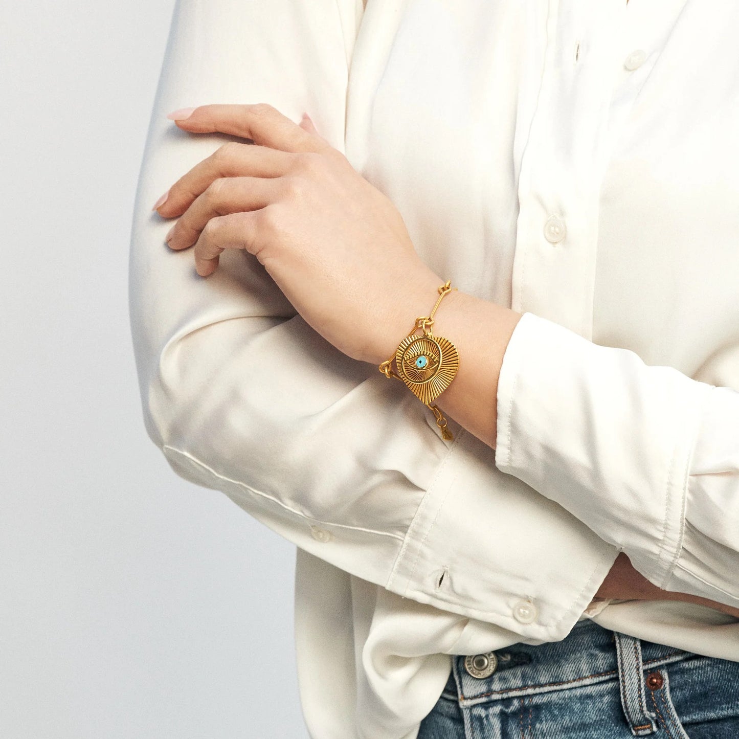 Gold bracelet with a blue gemstone on a person wearing a white shirt and jeans.