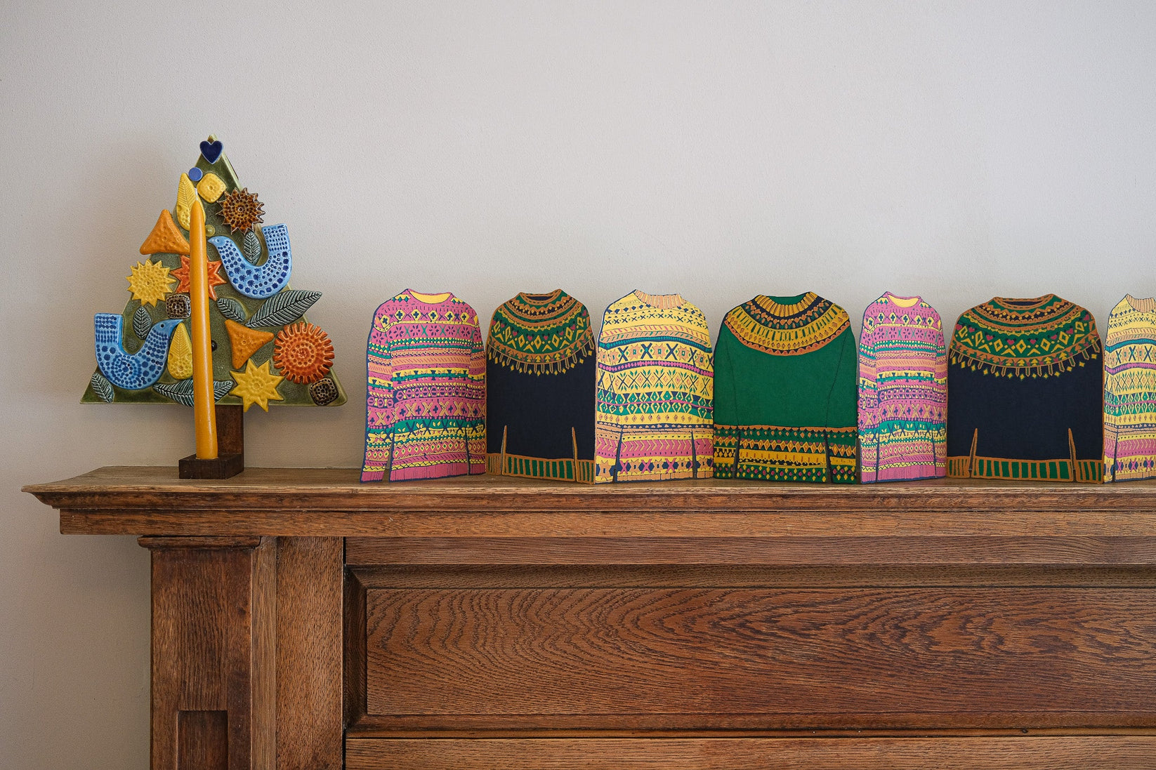 Colorful knitted sweaters on a wooden shelf with a decorative tree in the background.