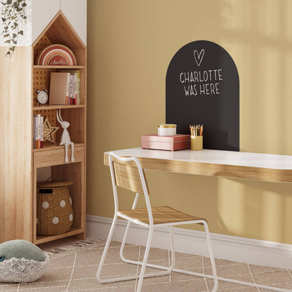Children's room with wooden desk, chair, and bookshelf against a yellow wall.