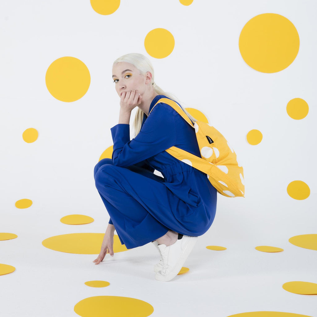 Person in blue outfit with yellow backpack against a polka dot background