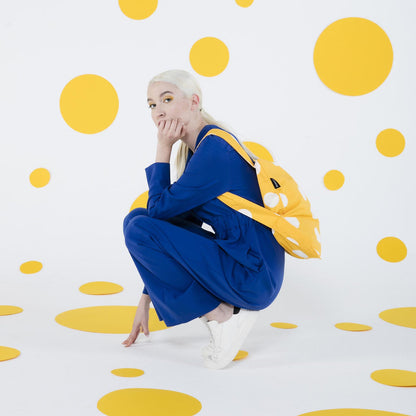 Person in blue outfit with yellow backpack against a polka dot background