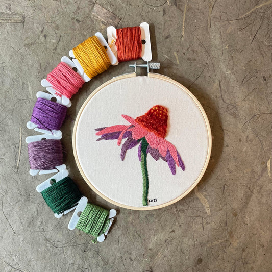 Embroidery hoop with a flower design and colorful threads on a textured surface