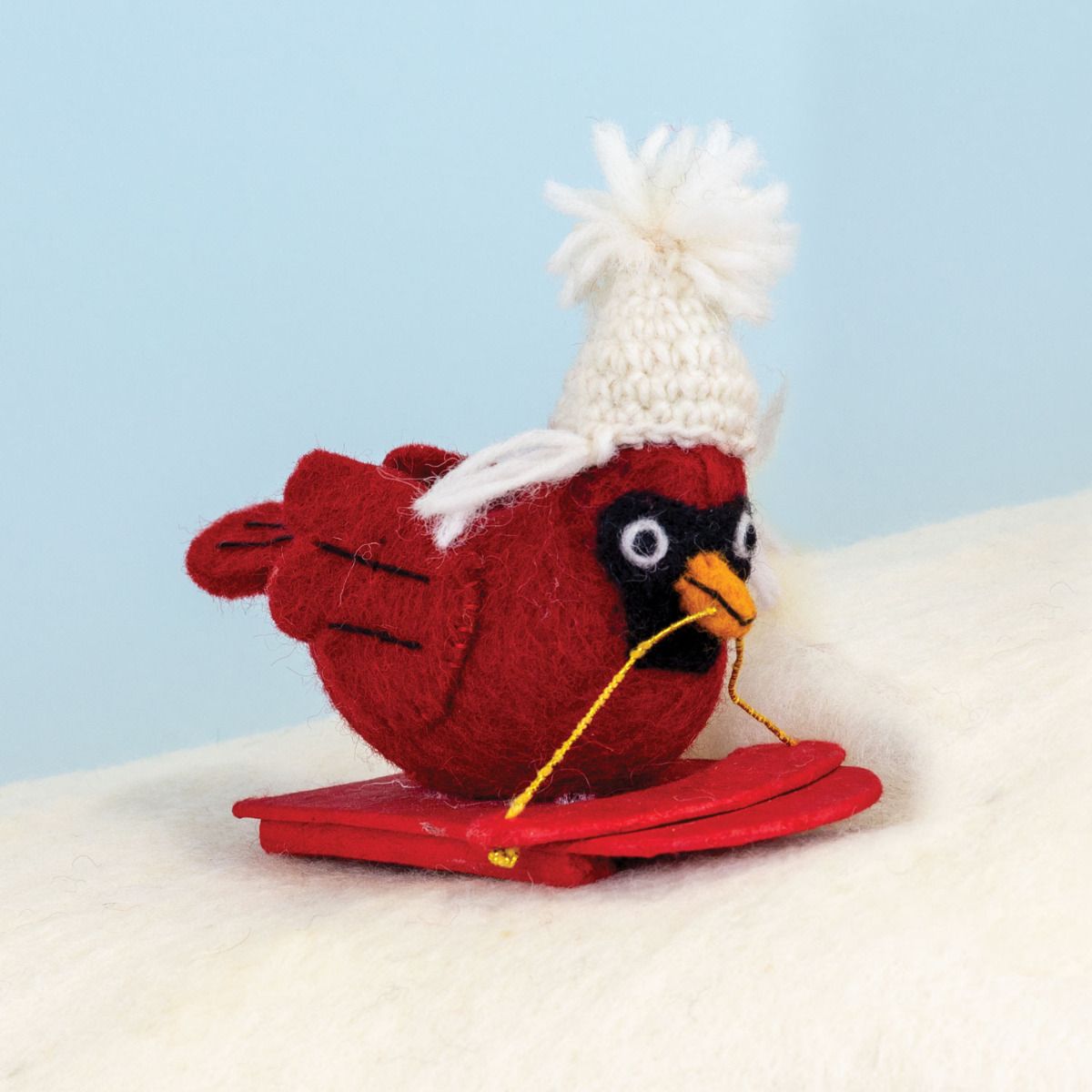 Knitted red cardinal bird with a white hat on a light blue background