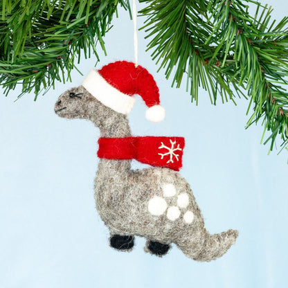 Dinosaur ornament with a Santa hat and red scarf hanging from a Christmas tree.
