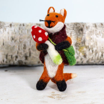 Felted fox ornament holding a red mushroom with a white background