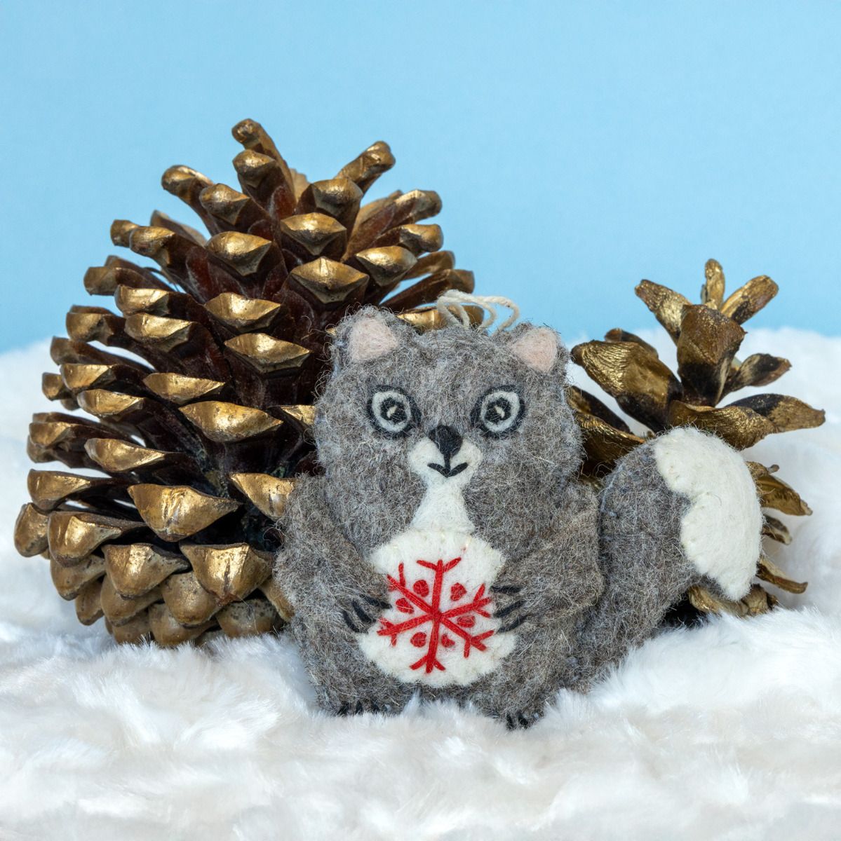 Plush ornament squirrel with a red snowflake on a snowy background with gold pinecones