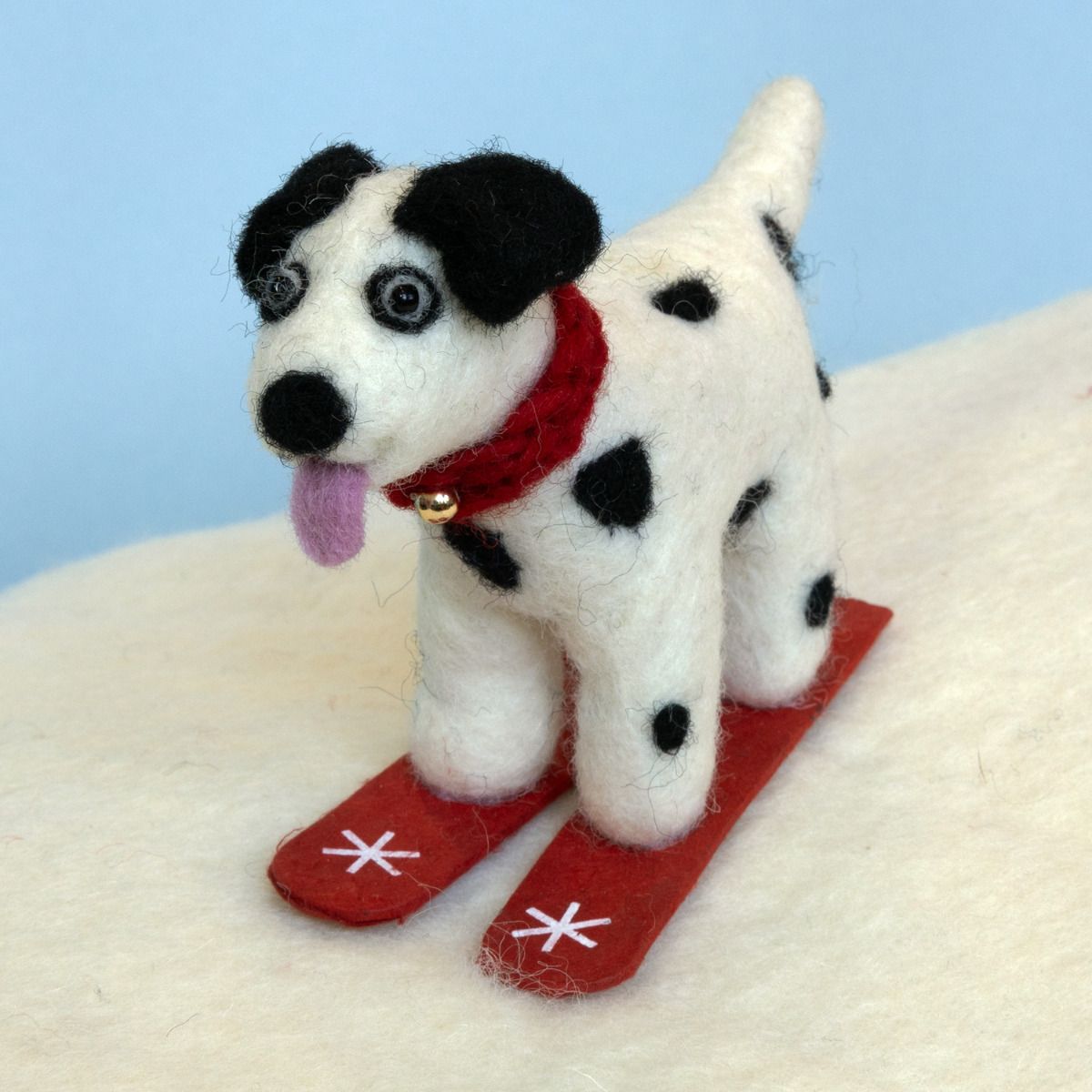 Stuffed dog toy with black spots wearing a red scarf and skis on a light blue background