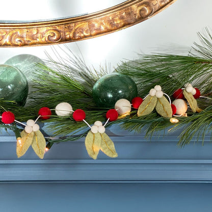 Decorative Christmas garland with green balls, red berries, and white flowers on a mantel.