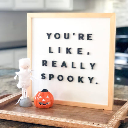 Letter board with 'YOU'RE LIKE, REALLY SPOOKY.' text on a wooden tray with Halloween decorations.
