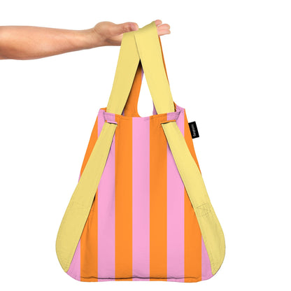 Colorful striped bag with yellow handles held by a person on a white background