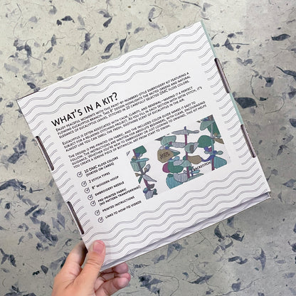 Hand holding a craft kit packaging with text and illustrations on a textured surface