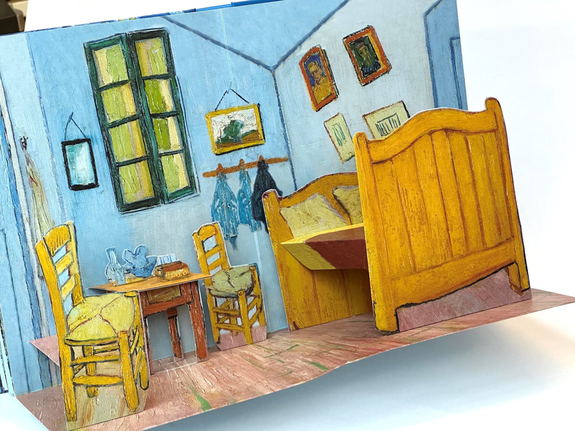 Pop-up book design inspired by Van Gogh's 'The Bedroom' with a bed, chairs, and framed pictures.