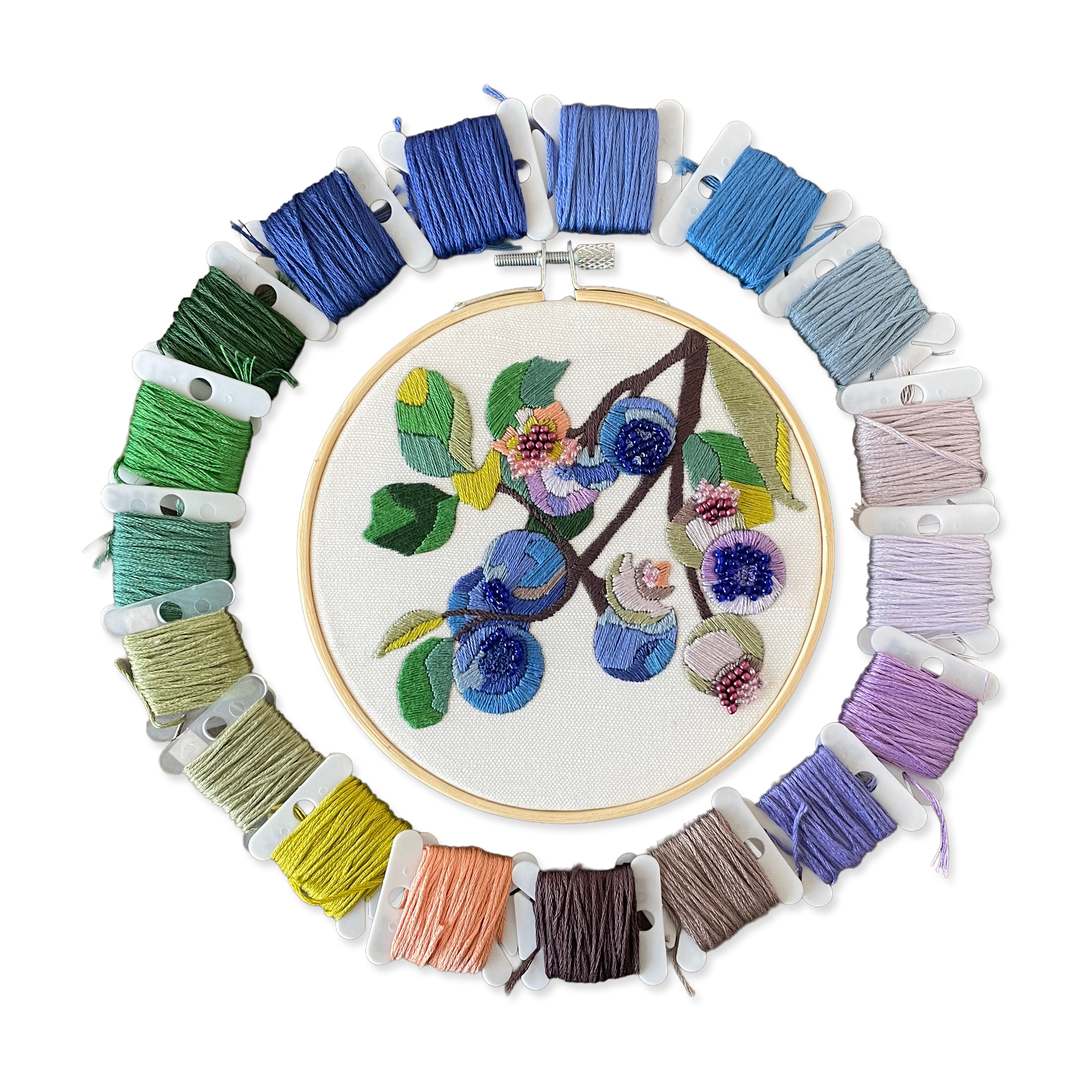 Embroidery hoop with floral design surrounded by colorful embroidery threads on a white background