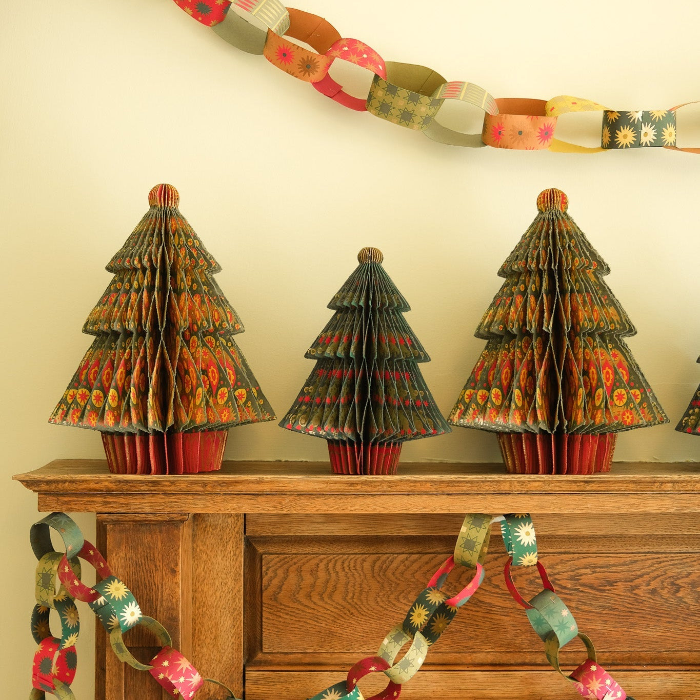 Decorative paper trees and garlands on a fireplace mantle.