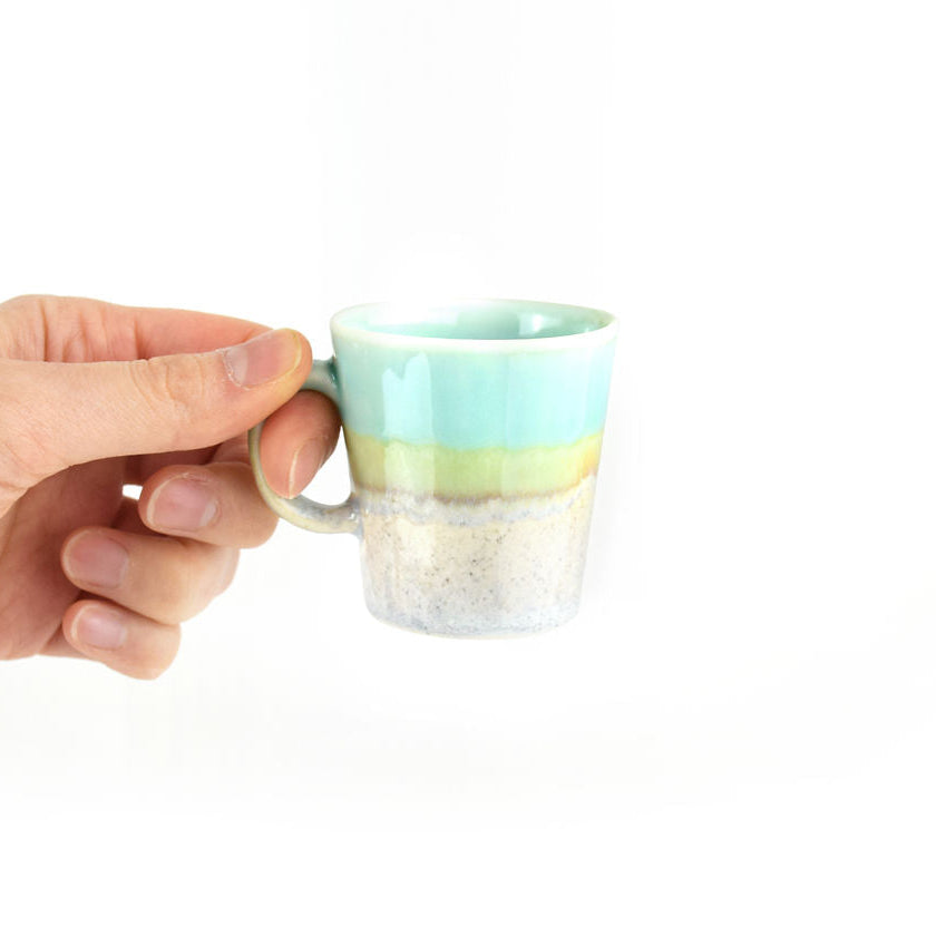 Hand holding a porcelain espresso cup with a pastel gradient design on a white background