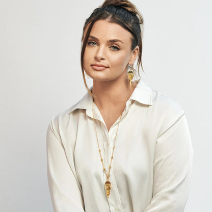 Woman wearing a white shirt and gold jewelry against a light gray background