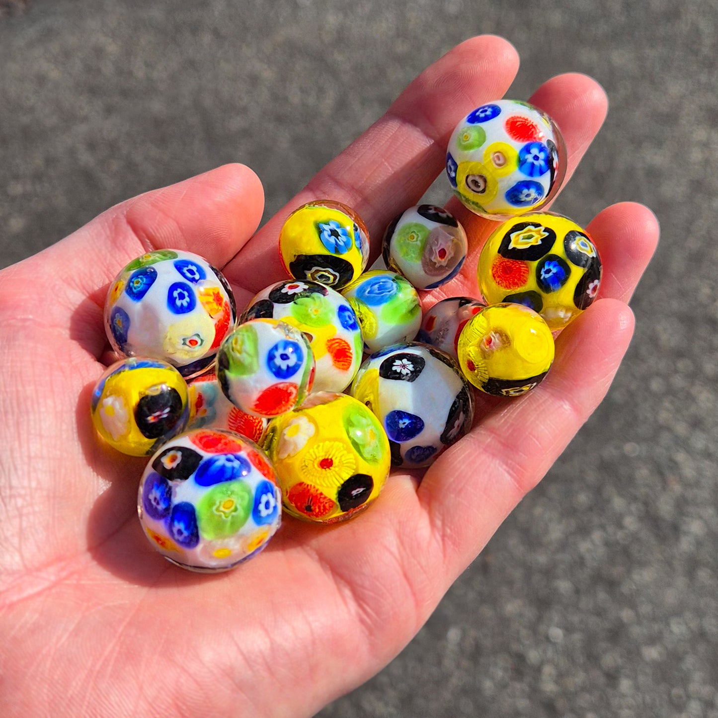Hand holding colorful glass marbles on a gray pavement background