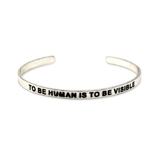 Silver cuff with the motto "To be human is to be visible."