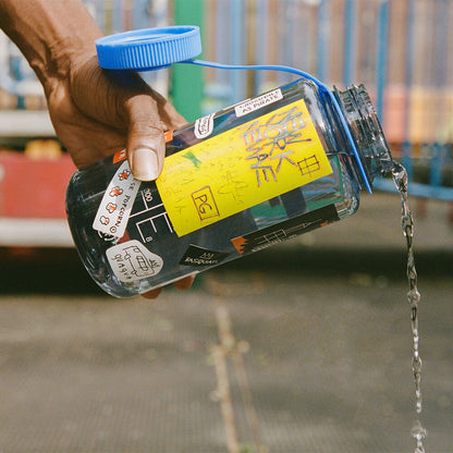 Photograph of a hand pouring water out of a water bottle decorated with stickers.