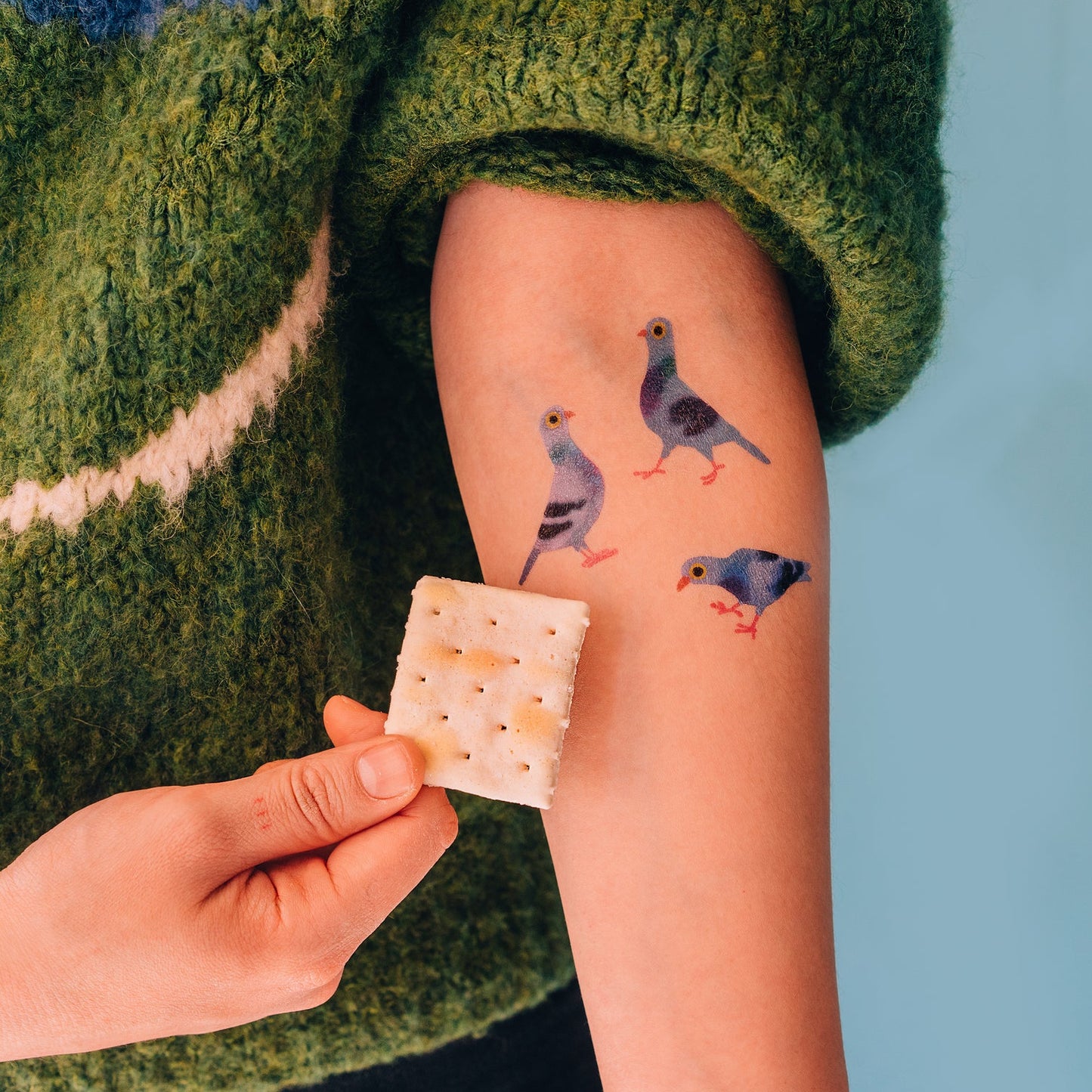 Person with temporary tattoos of birds on their arm, holding a cracker.