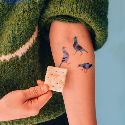Person with temporary tattoos of birds on their arm, holding a cracker.