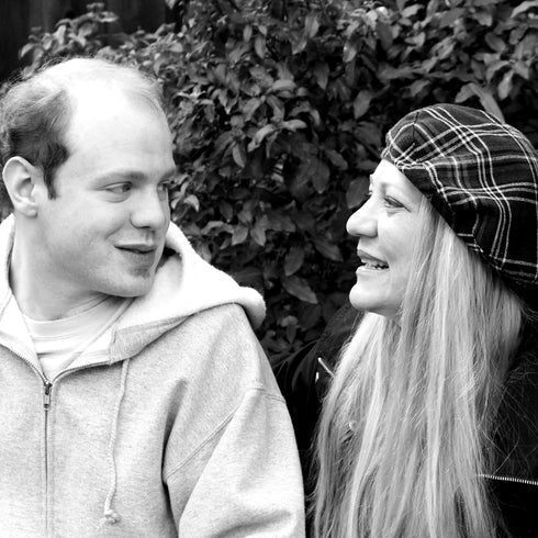Two people smiling at each other outdoors with a bush in the background