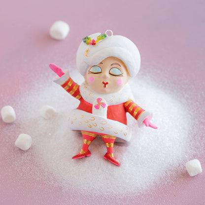 Decorative figurine of a snow maiden surrounded by marshmallows on a pink background