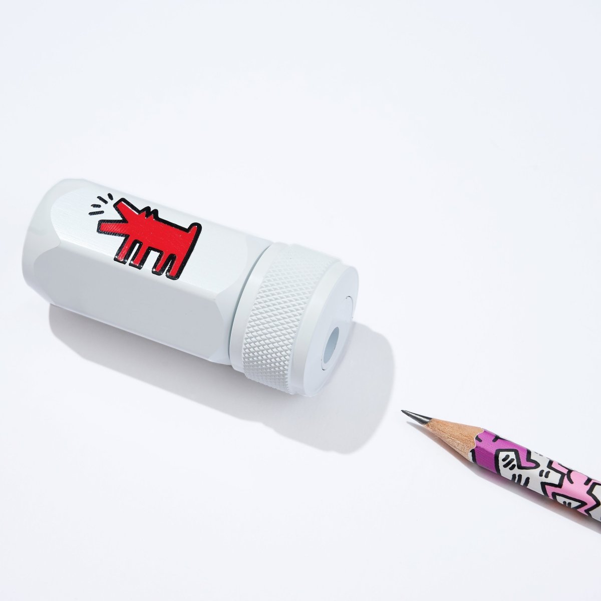 White cylindrical pencil sharpener with a red design next to a pencil on a white background