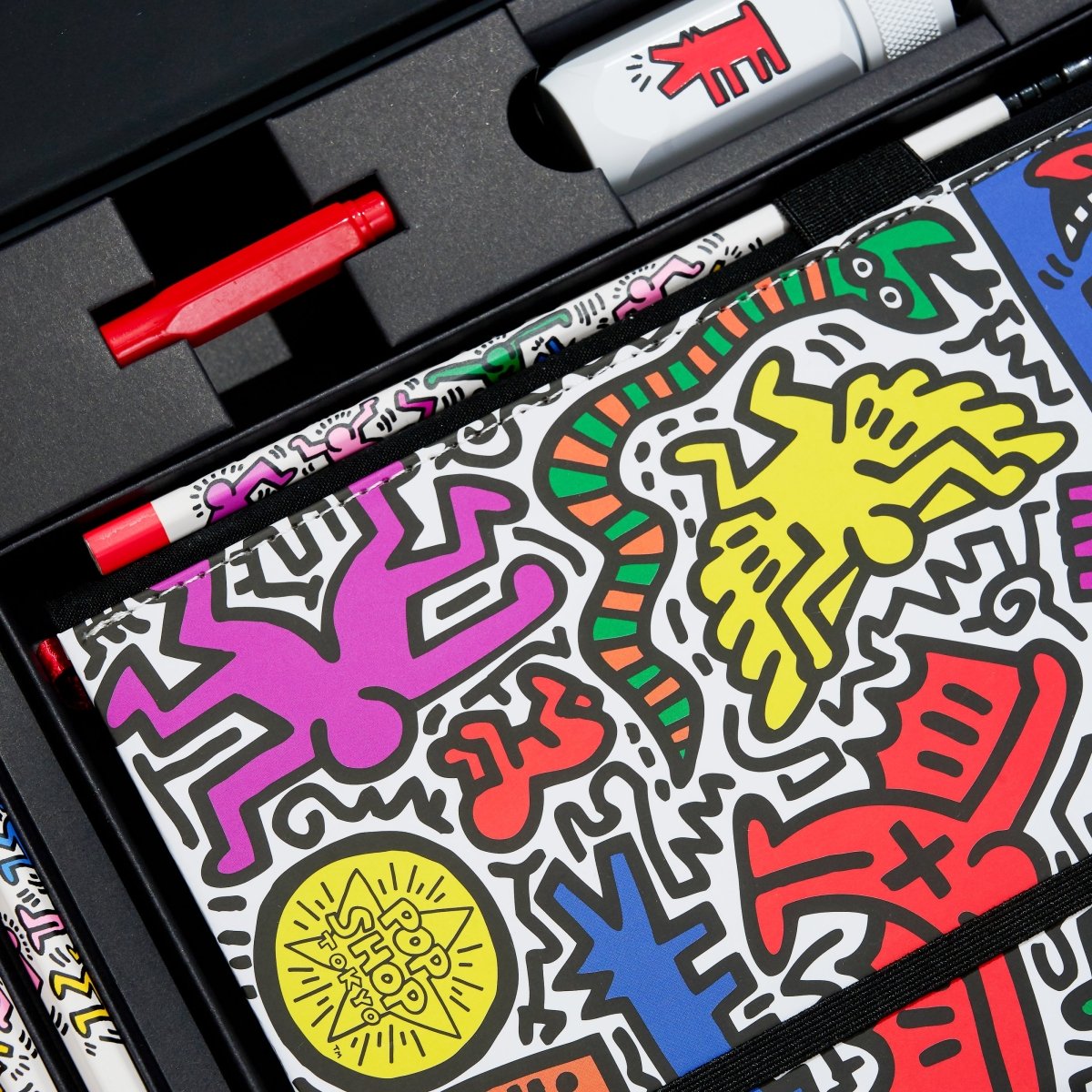 Colorful art supplies with Keith Haring-style designs in a black case.