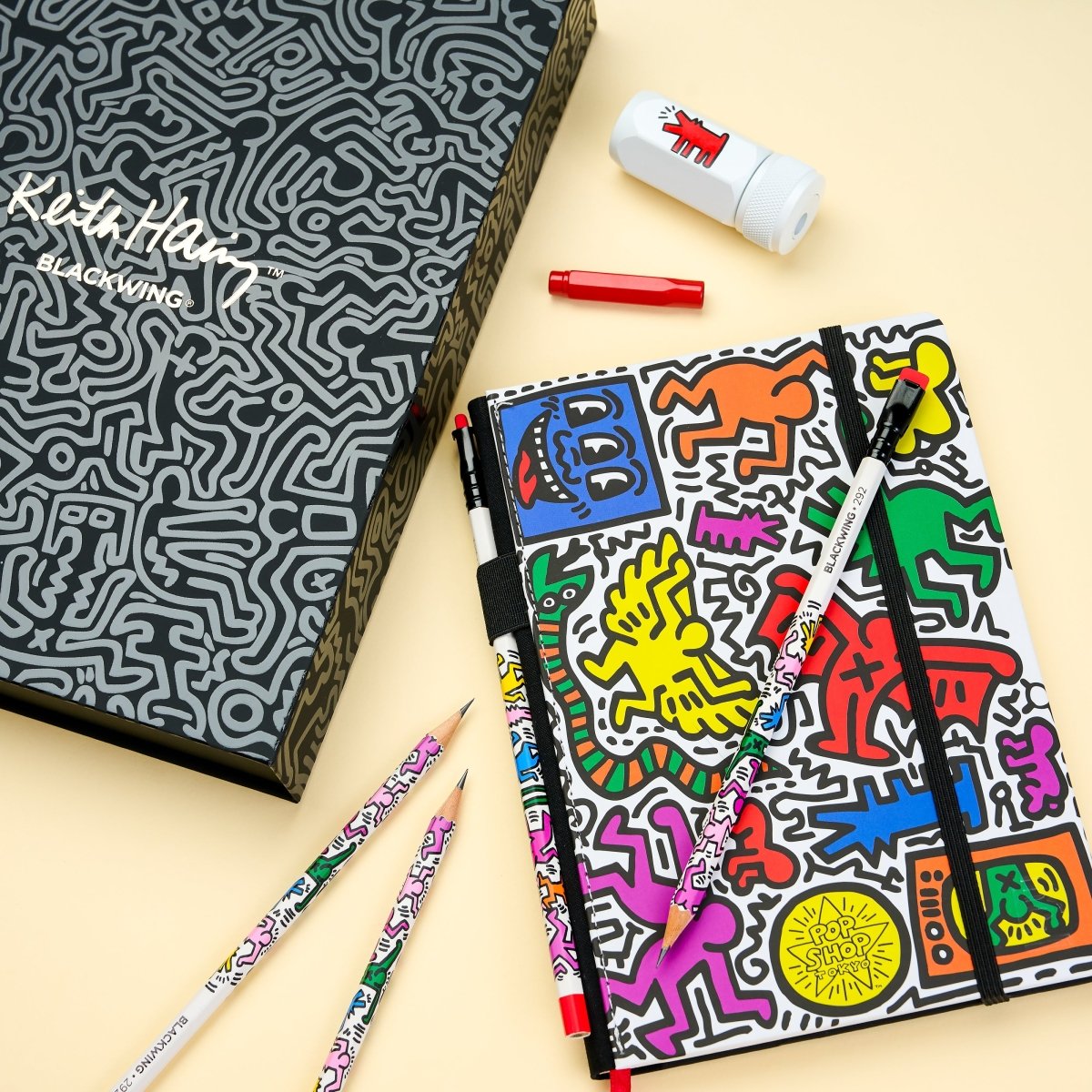 Keith Haring-themed stationery set with notebook, pencils, and eraser on a beige background