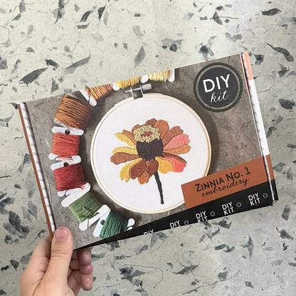 DIY embroidery kit packaging with a zinnia flower design on a textured surface