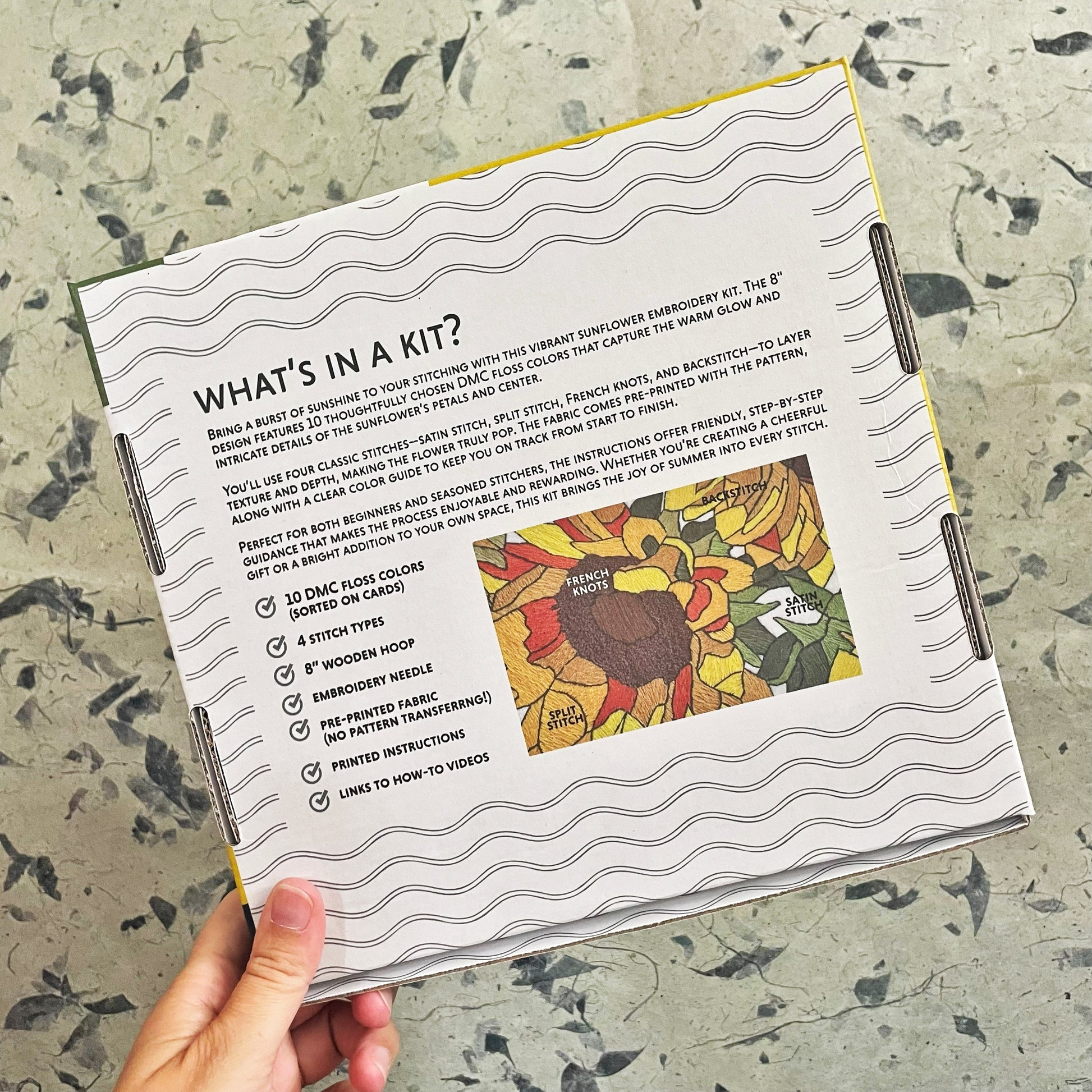 Embroidery kit packaging with text and sunflower design on a textured surface