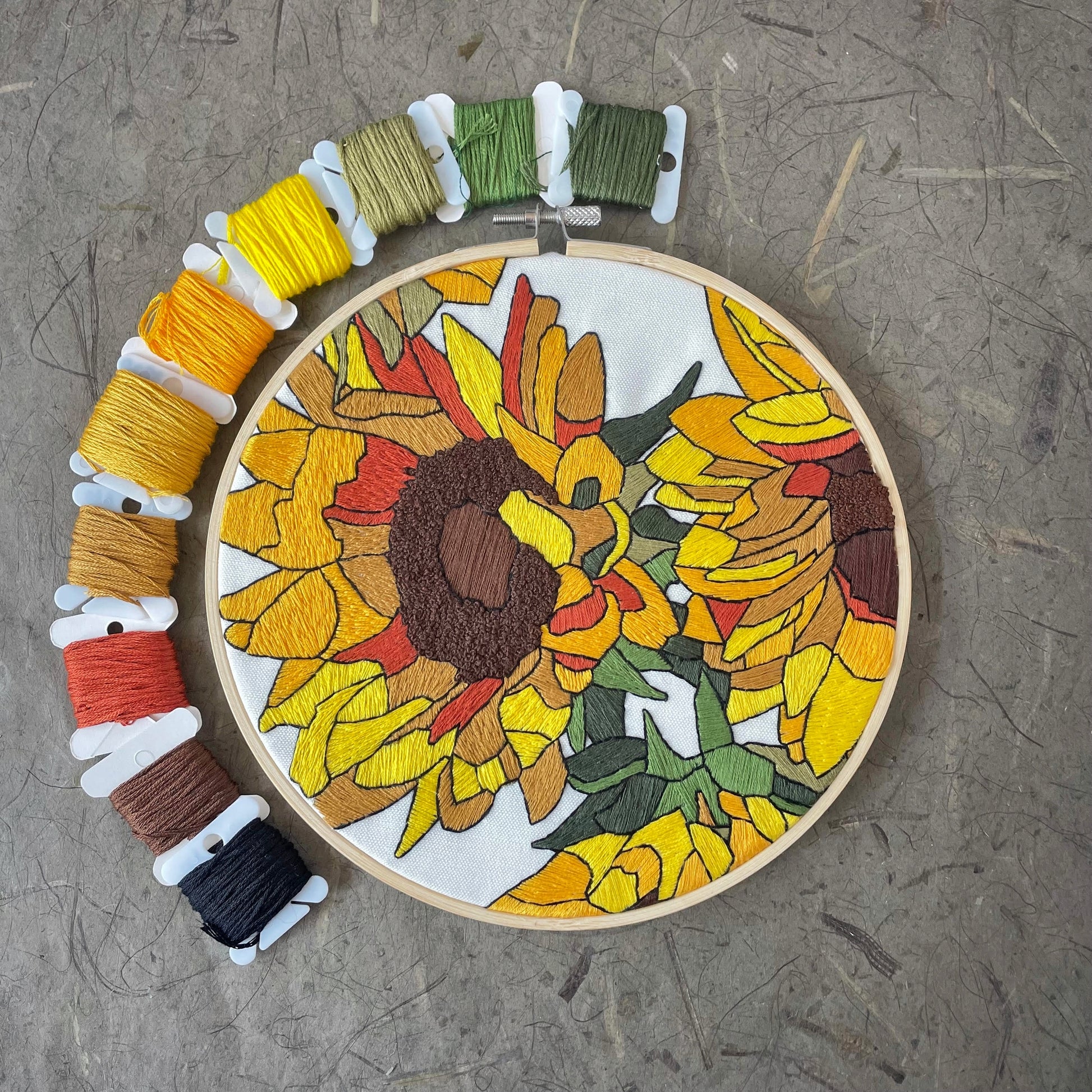 Embroidery hoop with a sunflower design and colorful threads on a textured surface