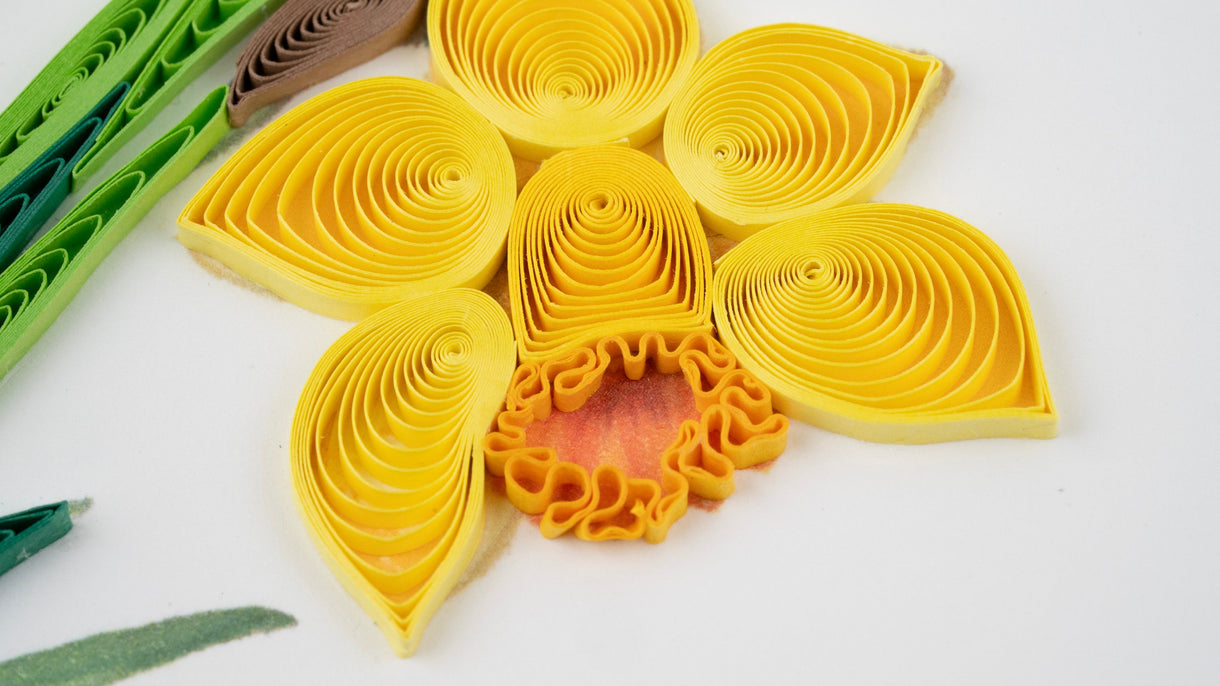Quilled paper flower with yellow petals and a red center on a white background