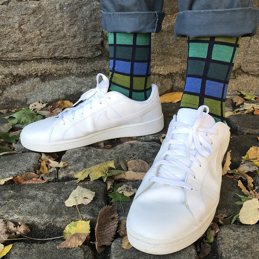 White sneakers worn with checkered socks on a stone surface with leaves.