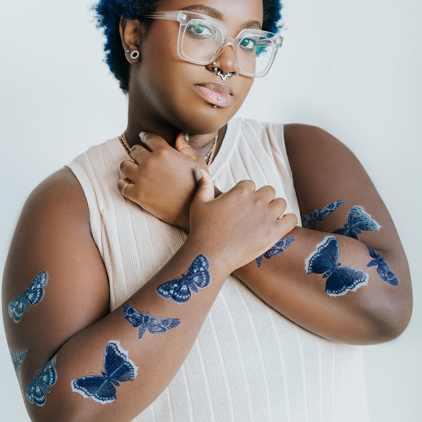 Person with blue moth tattoos on their arms against a white background