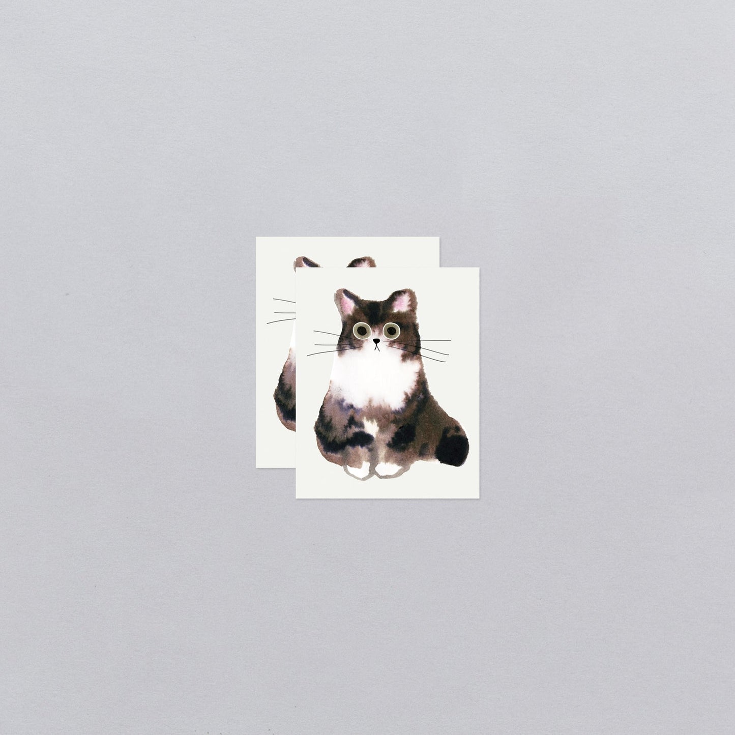 Two temporary tattoos with a cat illustration on a gray background