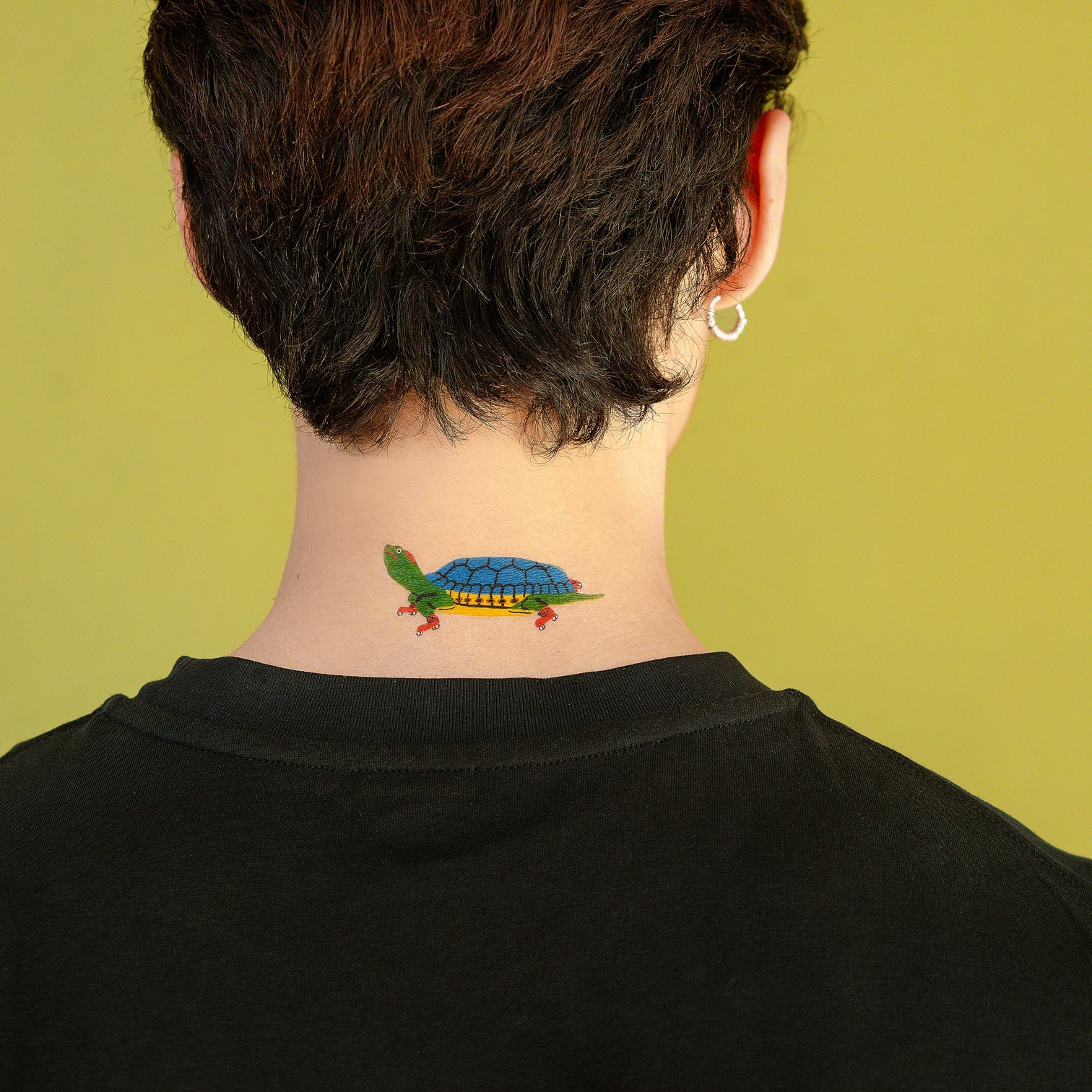 Person with a colorful turtle tattoo on their neck against a green background