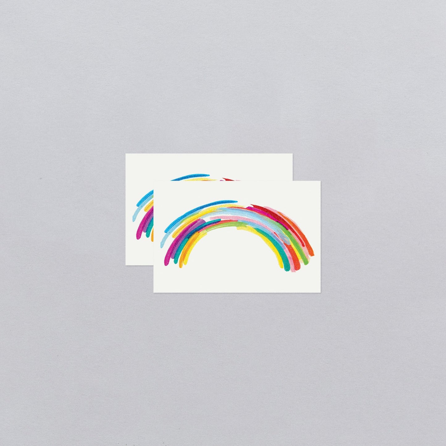 Two rainbow-shaped temporary tattoos on a gray background